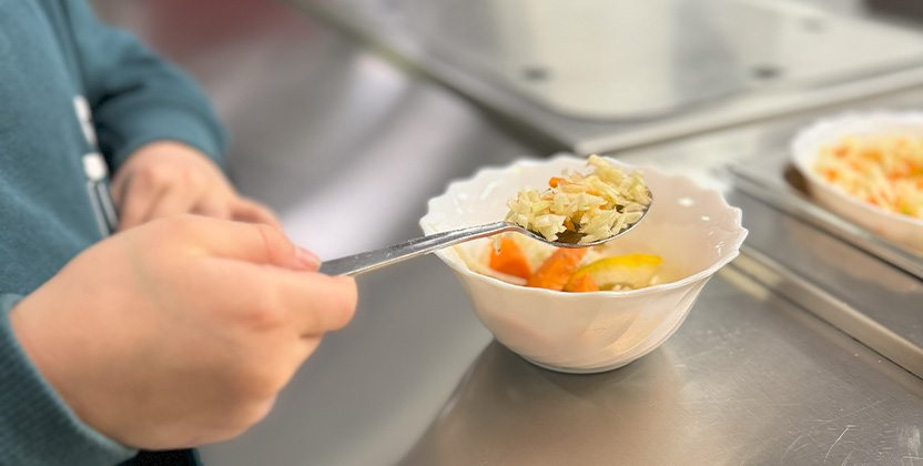 barnhand som håller i sked och lägger upp sallad i sen kål.