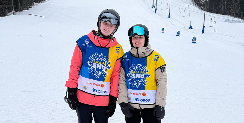 Två persoener med skidkläder i en skidbacke.