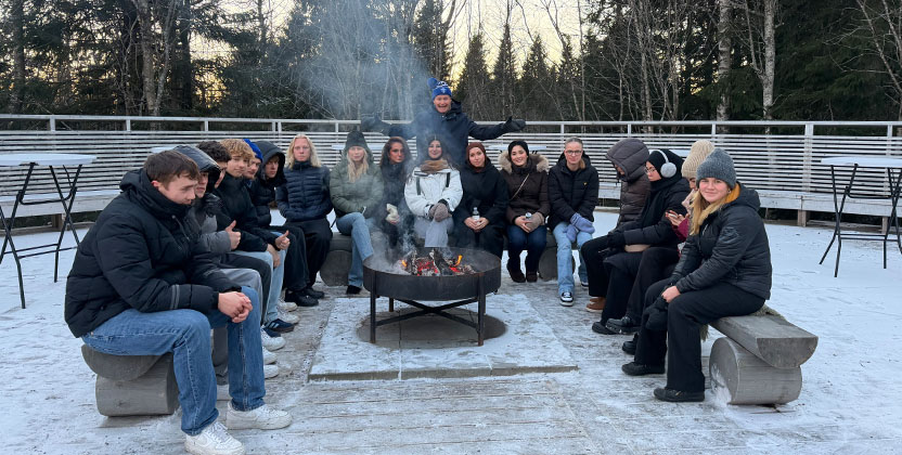 Elever och lärare som värmer sig vid en brasa.