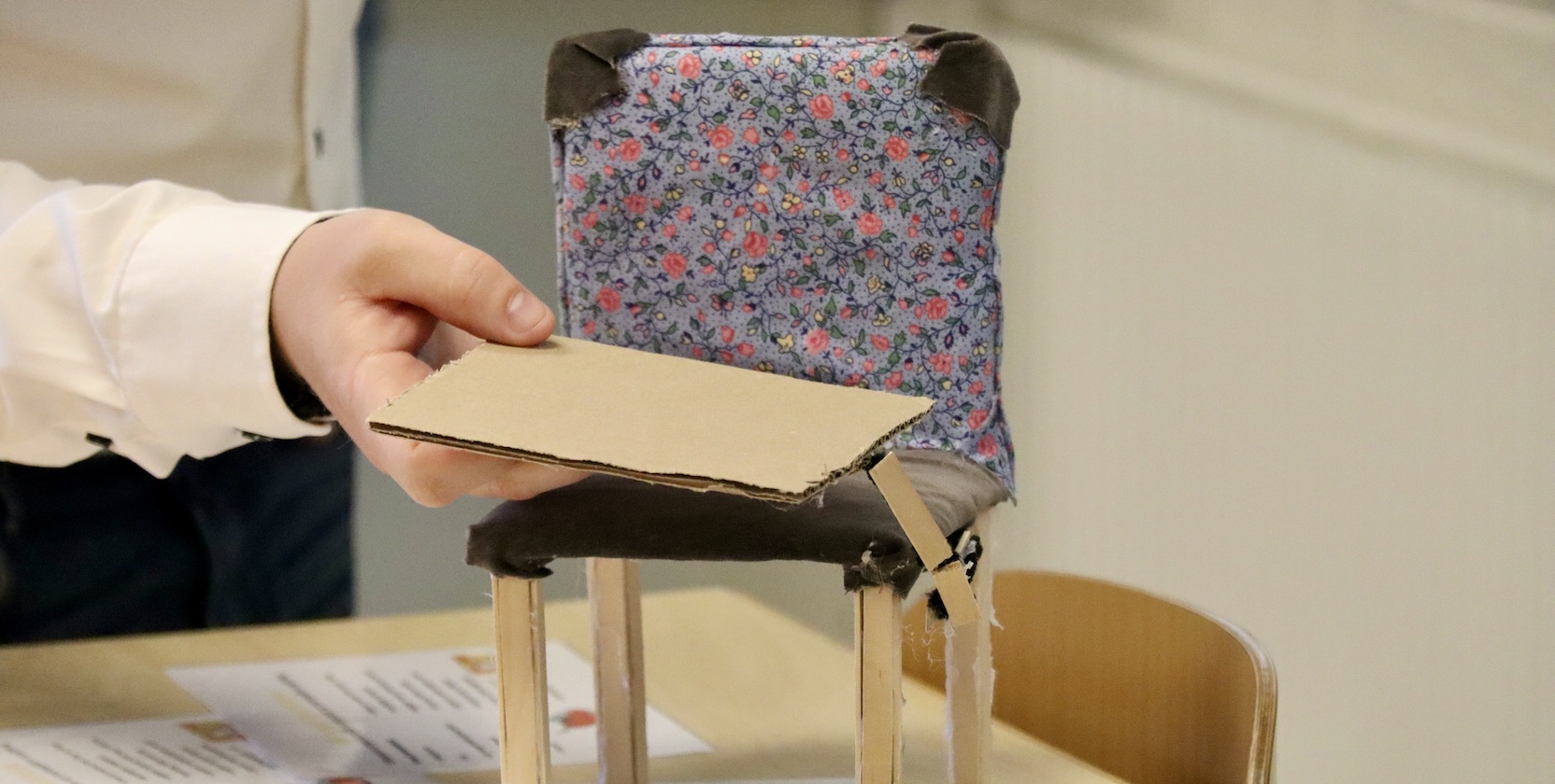 En prototyp i kartong av en stol med ett monterat sidobord, som också går att använda om fotstöd, står på en skolbänk.