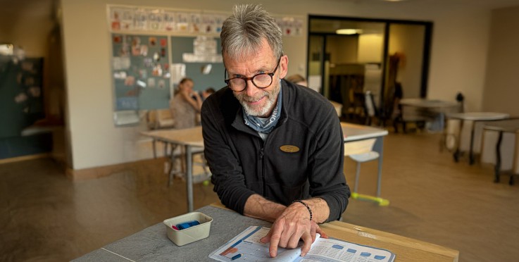 En person sitter vid ett bord i ett klassrum och pekar i en öppen bok.