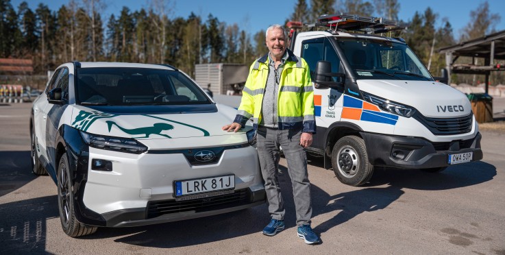 En person i reflexjacka står mellan två servicefordon på en asfalterad yta utomhus.