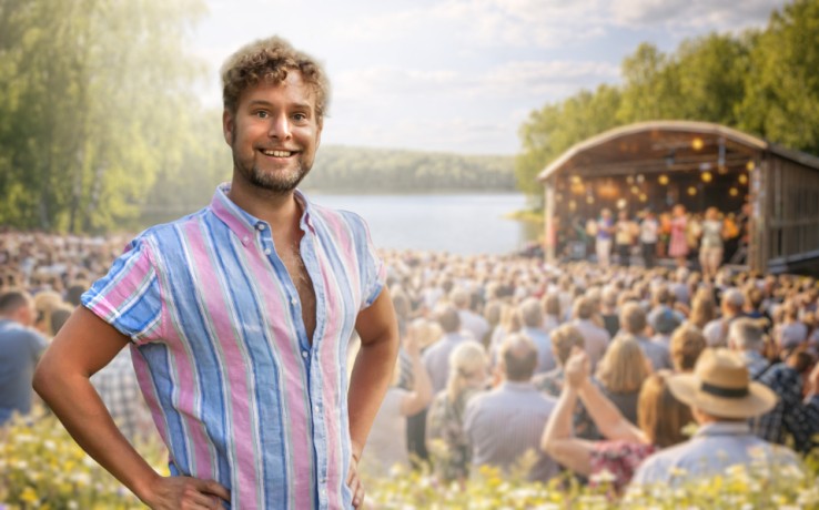 Person i randig skjorta står framför en stor publik vid en utomhusscen nära en sjö.