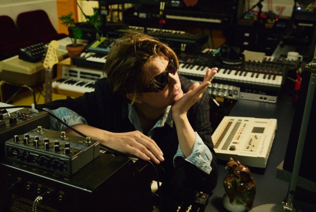 Person sitter i en studio omgiven av syntar, mixerbord och musikutrustning. Ansiktet är suddat.