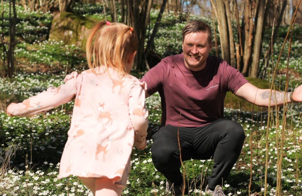Ett barn springer mot en vuxen med öppna armar i en blommande skog under våren.