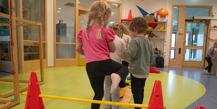 Flera barn leker och tränar motorik inomhus med hinderbanor på ett förskolegolv.