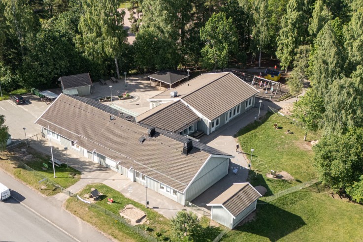 Flygfoto över ett bostadsområde med en större byggnad, omgiven av grönska och vägar.