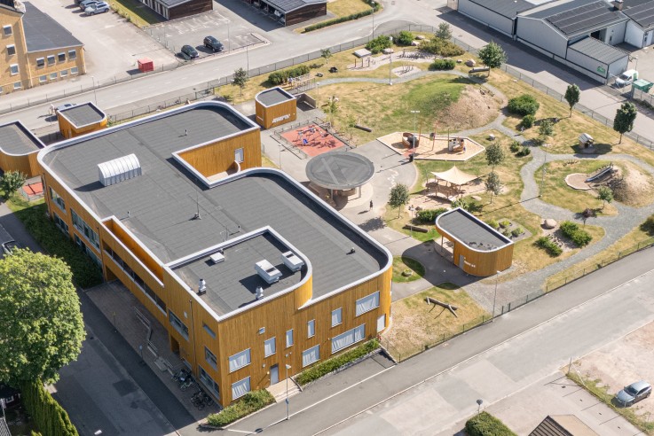 Flygbild över ett bostadsområde med skolbyggnad, lekplats och omgivande hus och industrier.