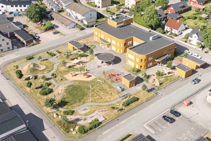 Flygfoto över ett bostadsområde med en modern skolbyggnad, lekplats och omgivande villor.