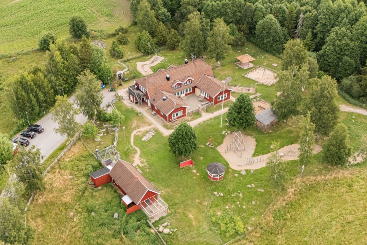 Flygfoto över en lantlig gård med röda hus, omgiven av grönska och skog.