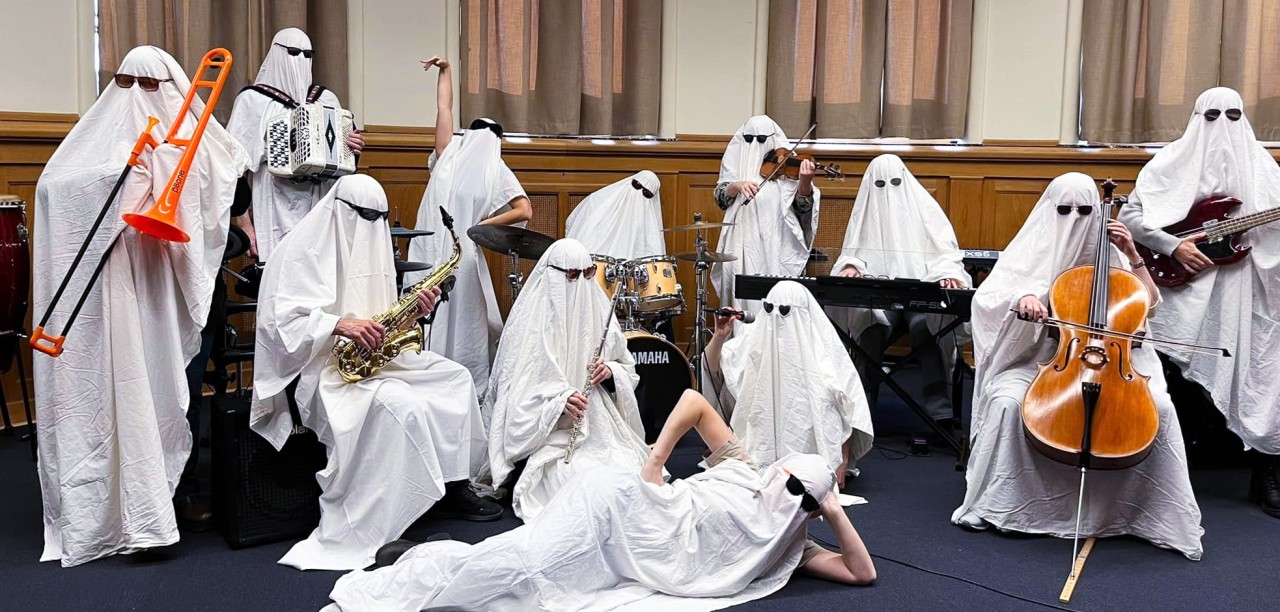 En grupp personer utklädda till spöken spelar olika musikinstrument i ett klassrum.