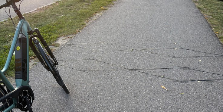 Cykel står vid en trottoar där flera svarta kablar ligger över gångbanan i kvällssol.