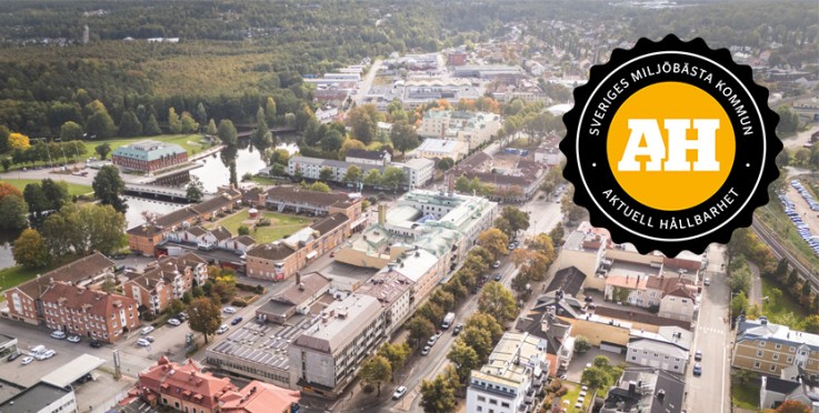 Flygbild över en svensk småstad med grönområden, byggnader och en miljöutmärkelse i förgrunden.