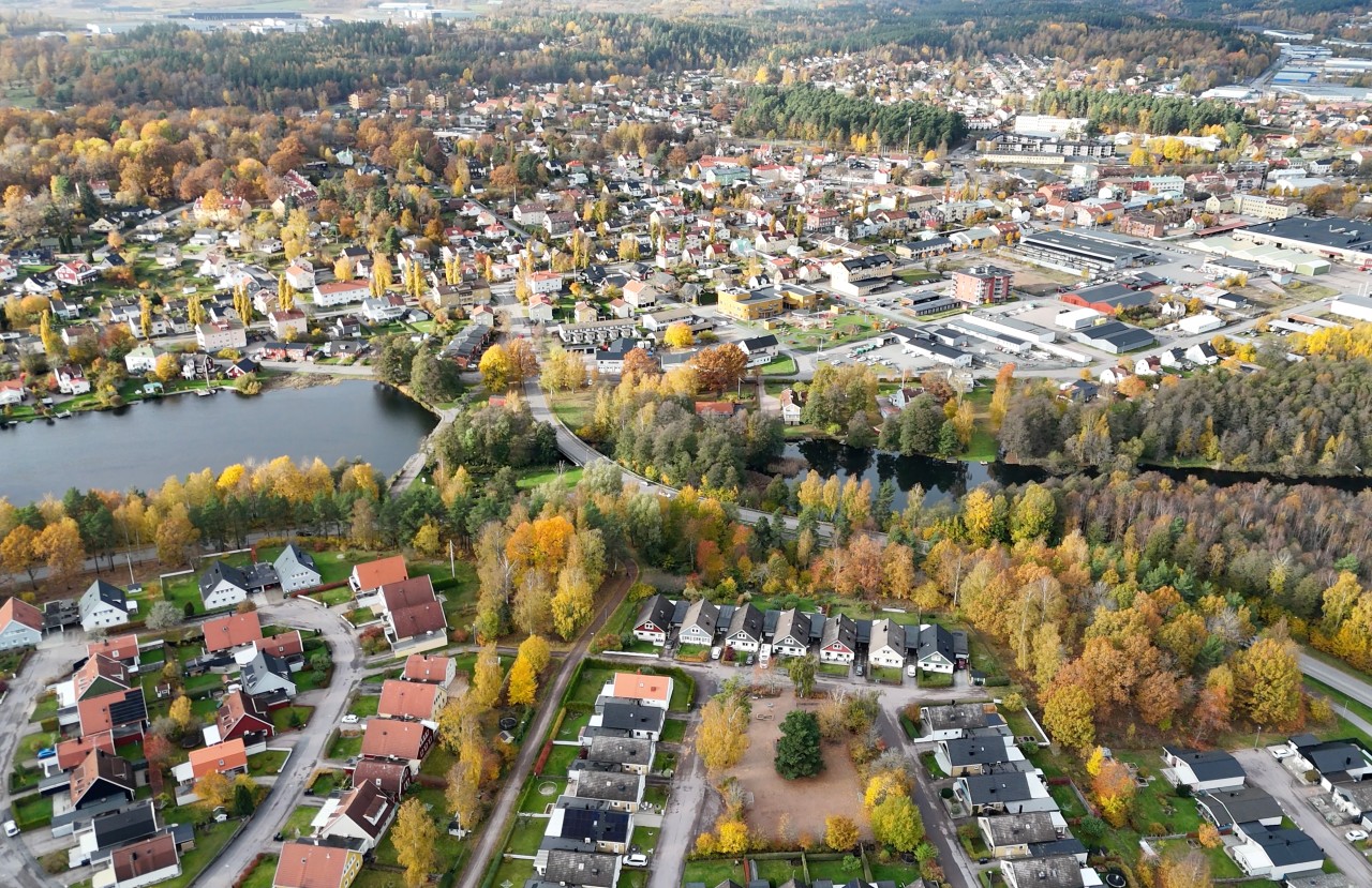 Flygbild över en småstad med hus, sjö, skog och höstfärger.